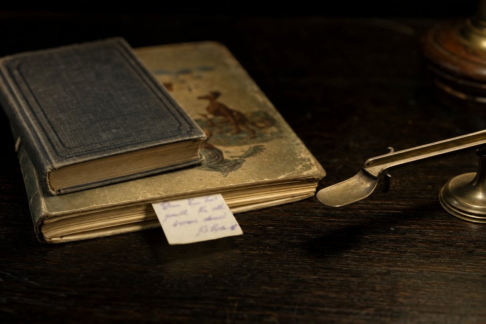 AI-generiertes Stillleben: zwei alte gebundene Bücher auf einem dunklen Schreibtisch, dazwischen ein handgeschriebener Antiquariatszettel, daneben eine Briefwaage aus Messing